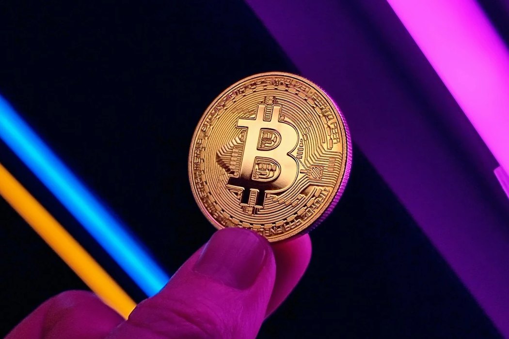 A gold Bitcoin coin held between two fingers